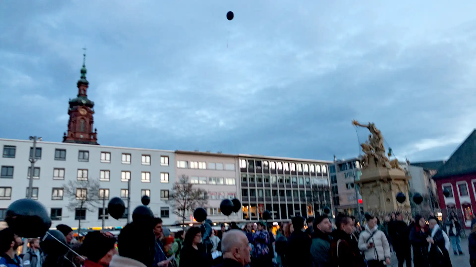 Bild von einer Menschenmenge auf dem Marktplatz mit schwarzen Luftballons. Oben im Bild schwebt ein Luftballon.