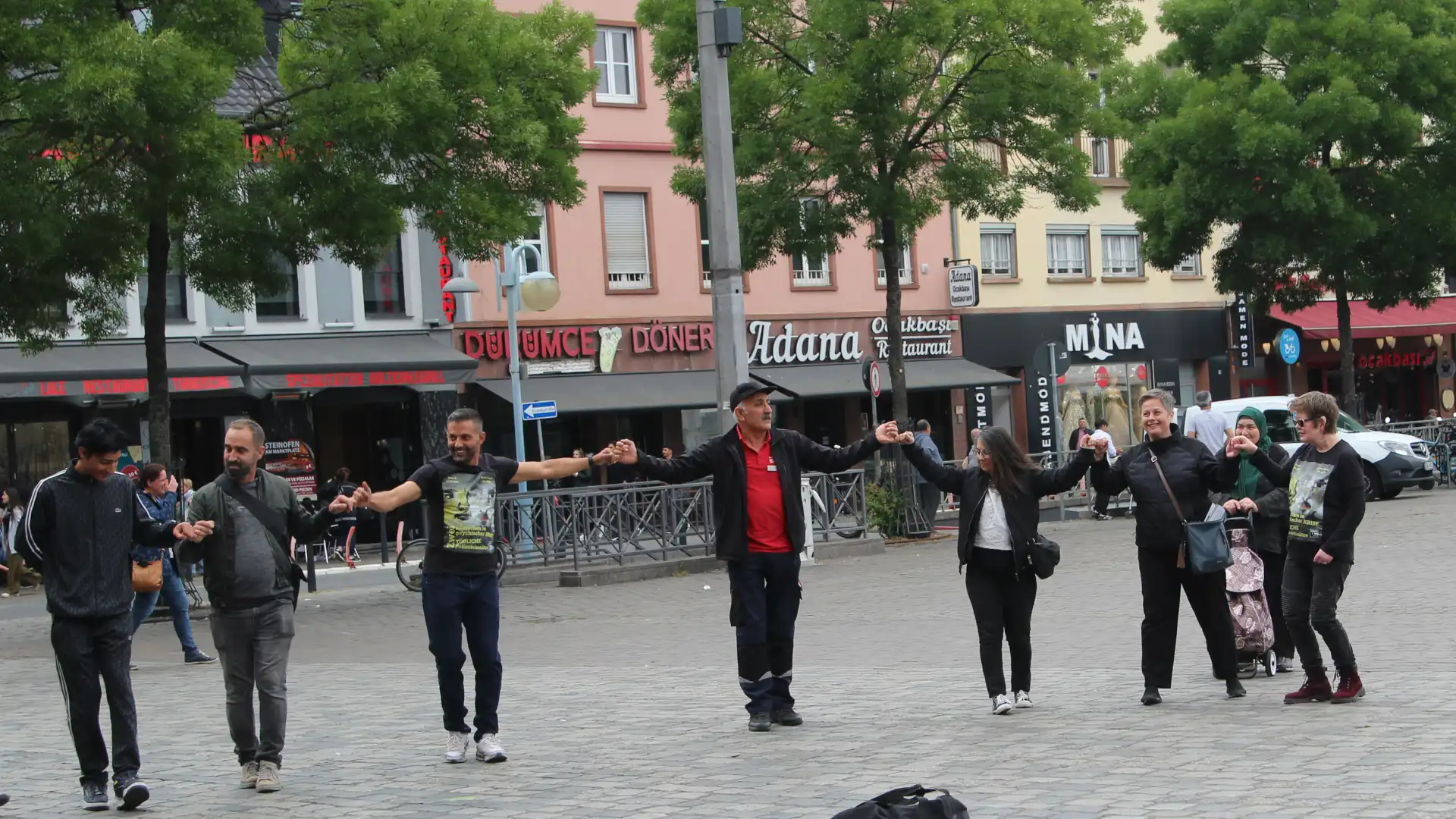 7 Personen tanzen auf dem Mannheimer Marktplatz Halay. Im Hintergrund ist die Geschäftszeile in Richtung Filsbach zu erkennen.